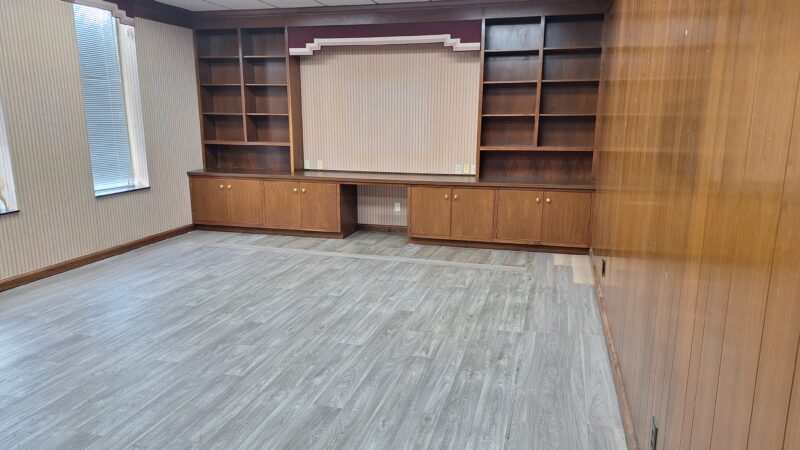 Empty office suite at 305 Plus Park Blvd in Nashville, TN, with built-in dark wood bookshelves and cabinets, wood-paneled accent wall, and gray vinyl plank flooring